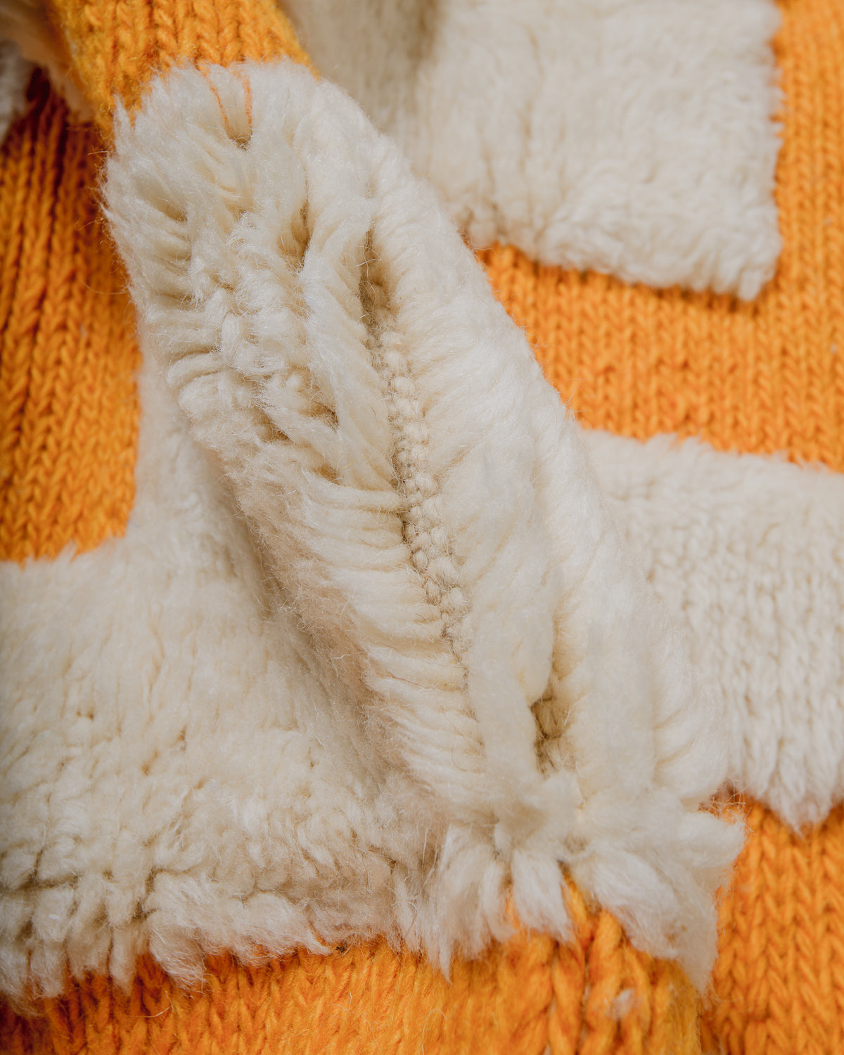 Close-up of a wool rug with thick cream pile and woven design in saffron yellow.
